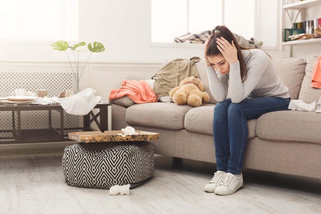 Desperate woman sitting on sofa in messy room