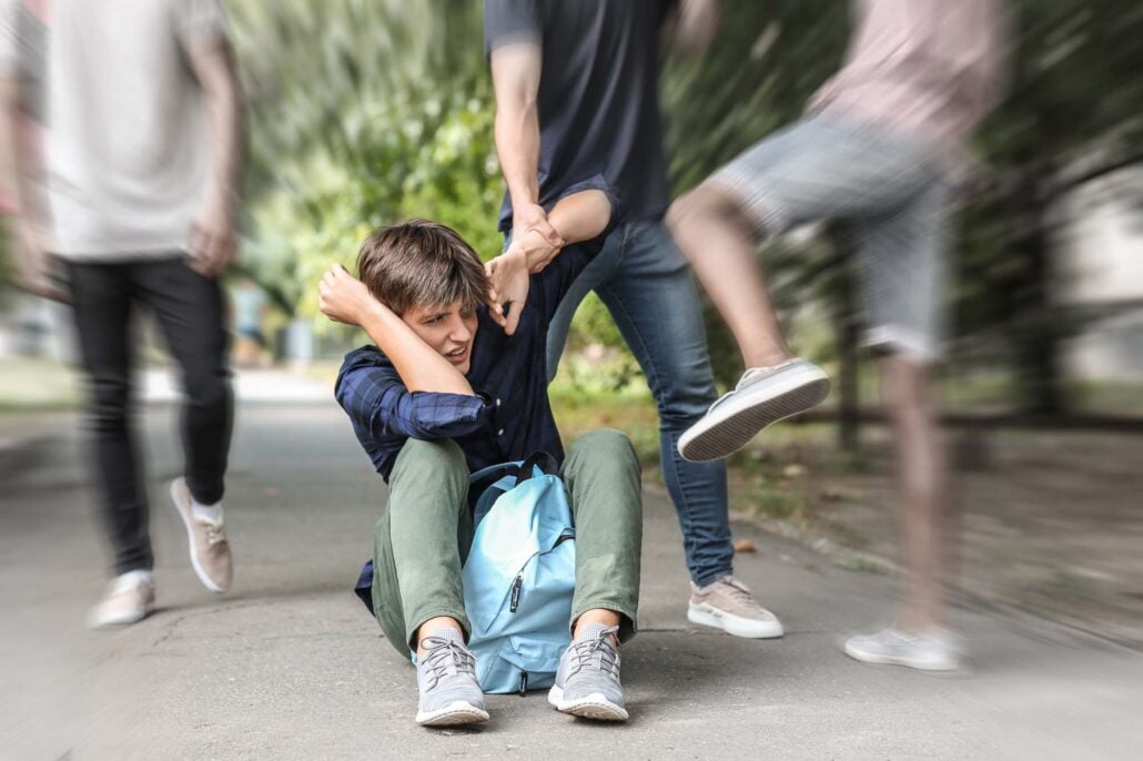 Aggressive teenagers bullying boy outdoors, view with motion blur effect